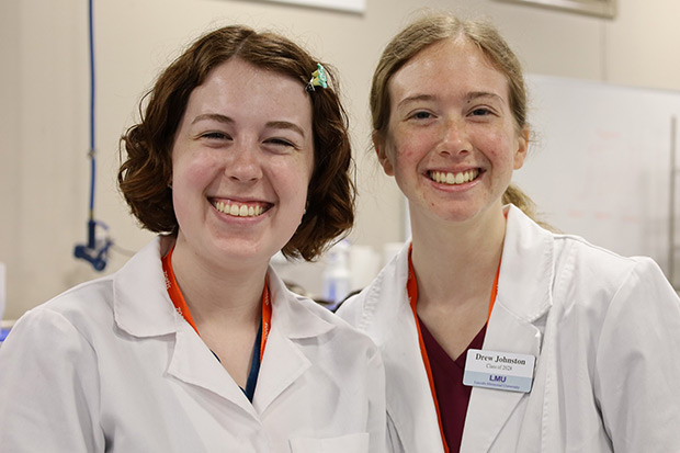 Two female veterinary students in white coats stand next to each other smiling