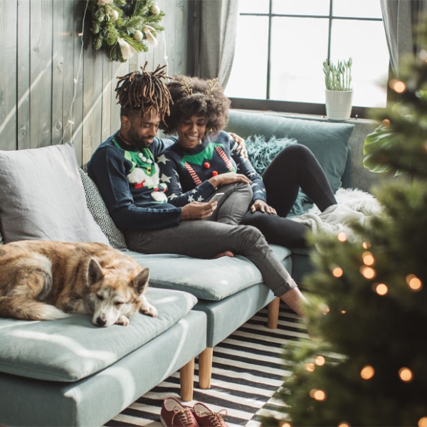 A man and woman lounge on their couch with their dog in front of a Christmas tree