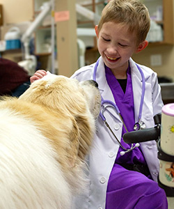 Young girl in scrubs and a white coat pets a dog