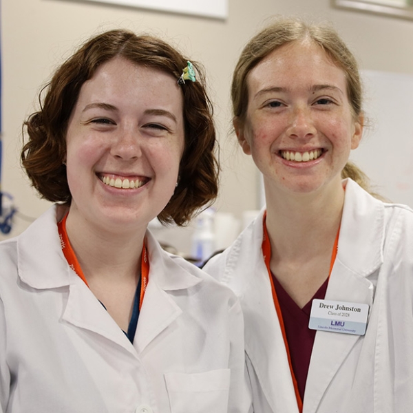 Two female veterinary students in white coats standing next to each other smiling